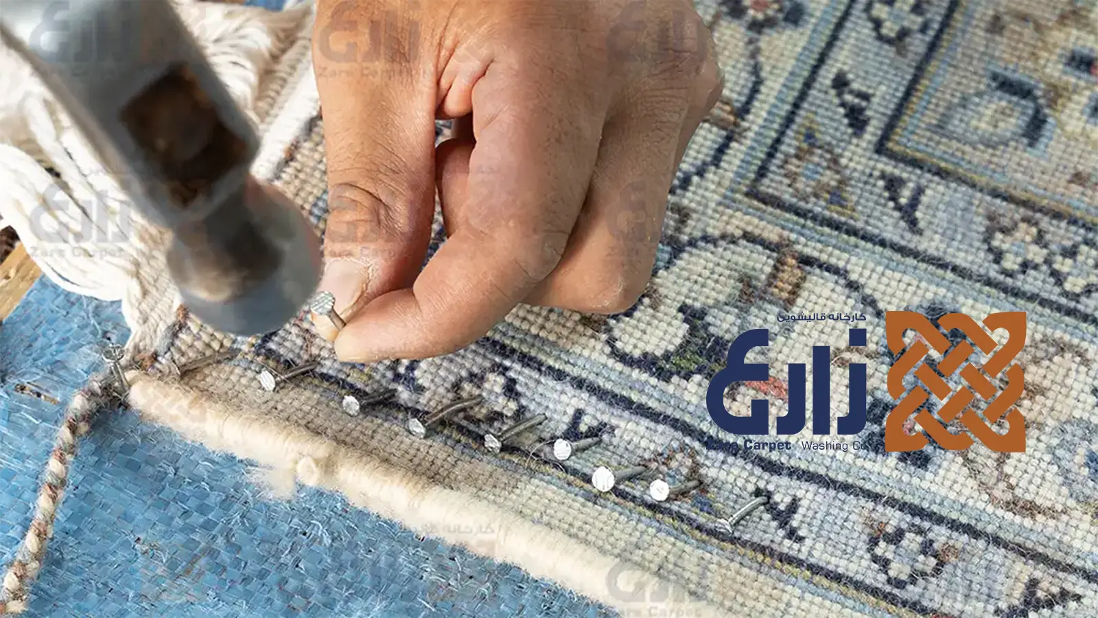 نمای نزدیک دست استادکار هنگام تثبیت لبه فرش دستباف با میخ و چکش روی سطح دارکشی