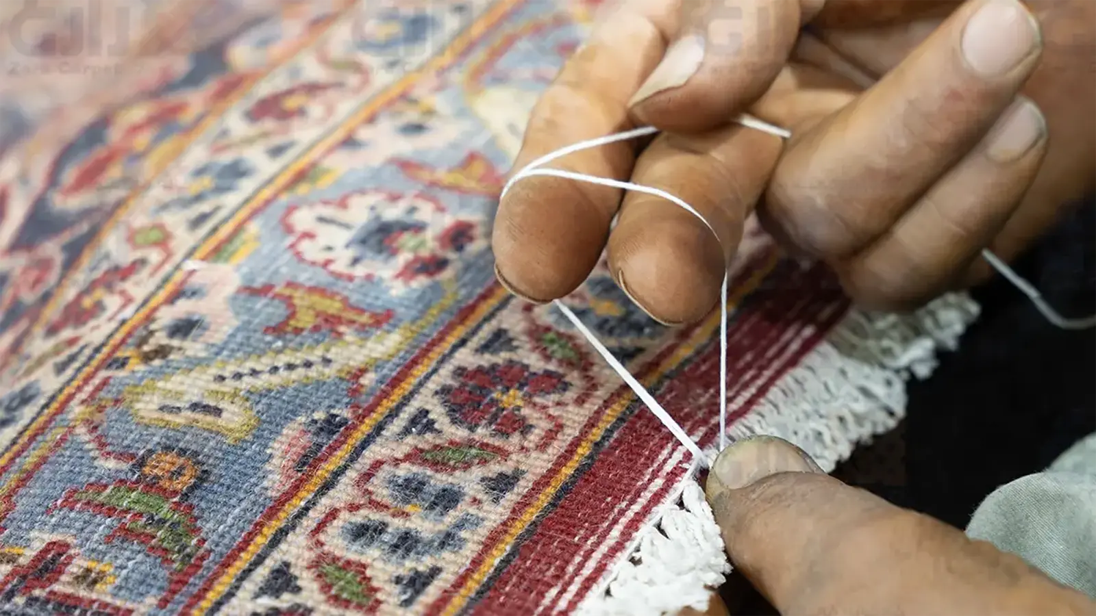 نمای نزدیک دست استادکار هنگام دوگره زدن ریشه فرش دستباف