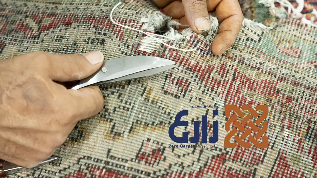 کار دستی با قیچی و نخ روی محدوده پارگی پشت فرش دستباف در کارگاه زارع